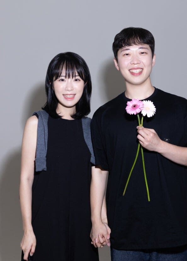 Couple standing against a plain backdrop holding flowers
